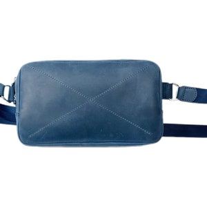 May include: A blue leather crossbody bag with a black adjustable strap. The bag has a flap closure and a stitched X design on the front.