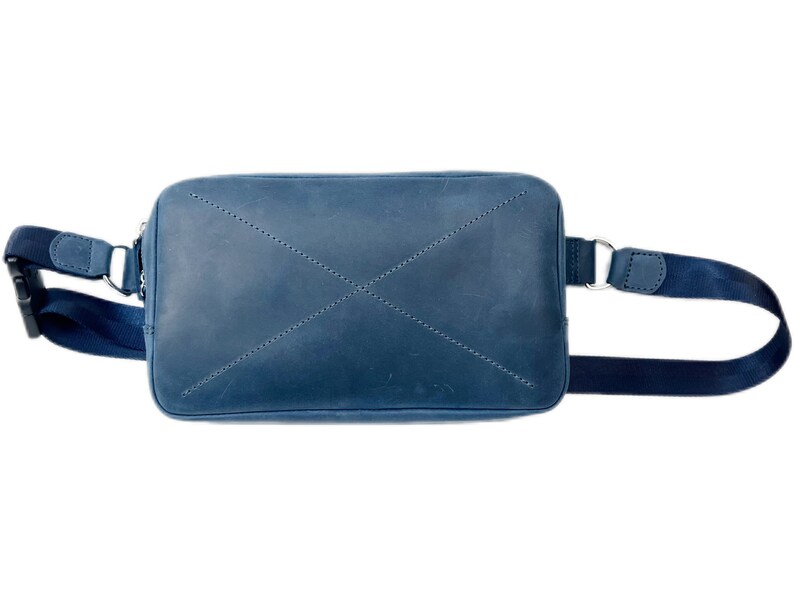 May include: A blue leather crossbody bag with a black adjustable strap. The bag has a flap closure and a stitched X design on the front.