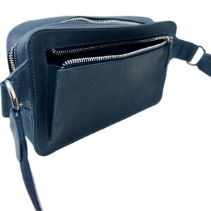 May include: A dark blue leather fanny pack with a zipped pocket on the front and a long adjustable strap.