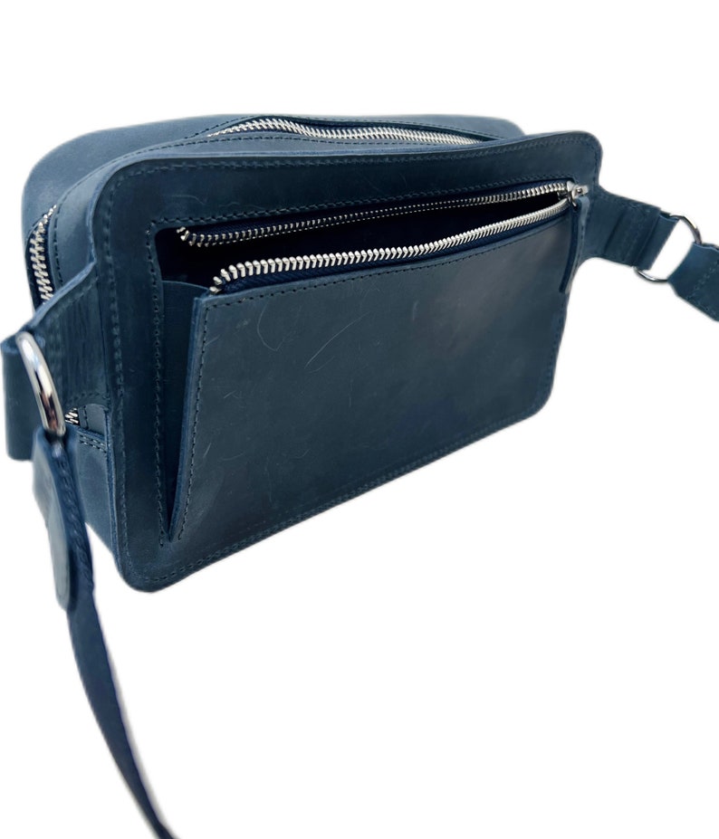 May include: A dark blue leather fanny pack with a zipped pocket on the front and a long adjustable strap.