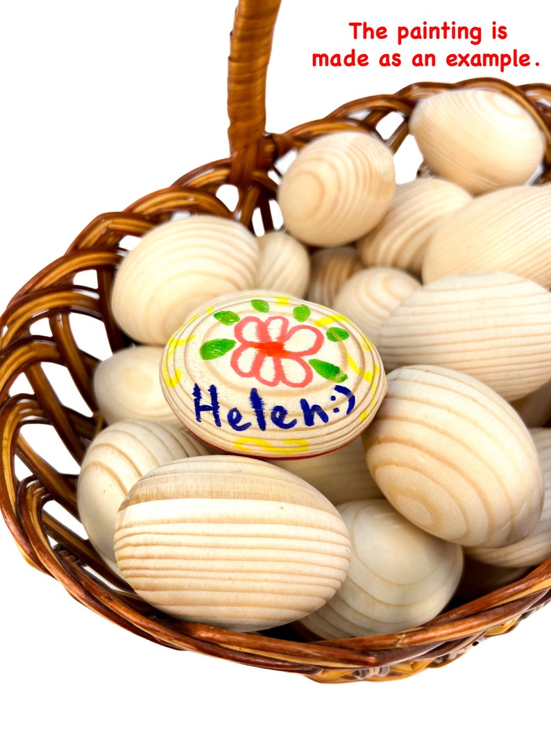 K&ouml;nnte beinhalten: Ein Weidenkorb gef&uuml;llt mit Holzeiern. Ein Ei ist mit einem rot-gr&uuml;nen Blumenmuster und dem Namen "Helen" in Blau bemalt. Der Text "The painting is made as an example" ist sichtbar.