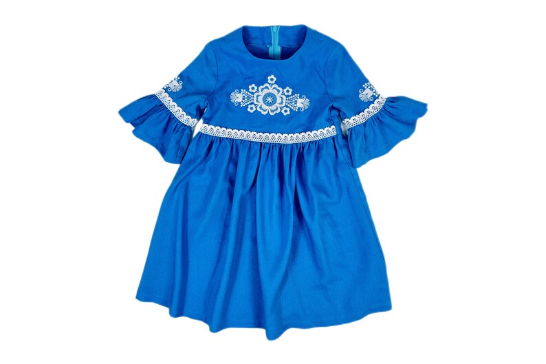 K&ouml;nnte beinhalten: Ein blaues Kleid mit wei&szlig;en gestickten Blumen und Spitzenbesatz. Das Kleid hat einen runden Ausschnitt und 3/4 &Auml;rmel.