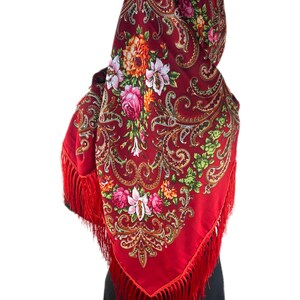 May include: A red shawl with a floral pattern and gold accents. The shawl has a fringe border and is worn over the head.