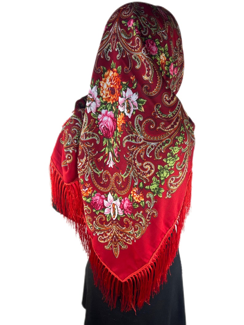 May include: A red shawl with a floral pattern and gold accents. The shawl has a fringe border and is worn over the head.
