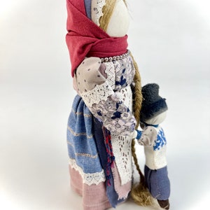 May include: A handmade fabric doll with a red headscarf and a long braid, holding the hand of a smaller doll wearing a blue hat and a blue and white patterned shirt.