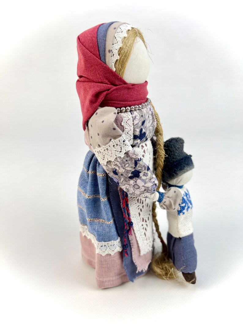 May include: A handmade fabric doll with a red headscarf and a long braid, holding the hand of a smaller doll wearing a blue hat and a blue and white patterned shirt.