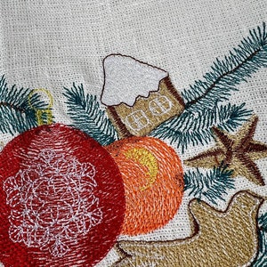 May include: Embroidered Christmas tree skirt with festive ornaments. Features a red ornament with a white snowflake design, an orange ornament, a gingerbread house, a star, a dove, and green pine needles. The design is on a cream-colored fabric.