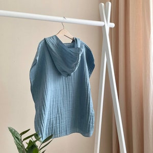 Puede incluir: Una toalla con capucha de color azul claro colgada de un estante de madera blanco. La toalla tiene una textura de gofre y est&aacute; hecha de un material suave y absorbente.