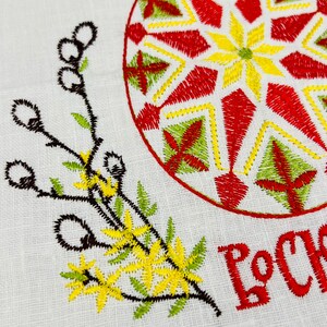 May include: Embroidered white fabric with a large, decorated Easter egg in red, yellow, and green. The text "Christ is Risen" is embroidered in red. Floral and branch embroidery in yellow and green.