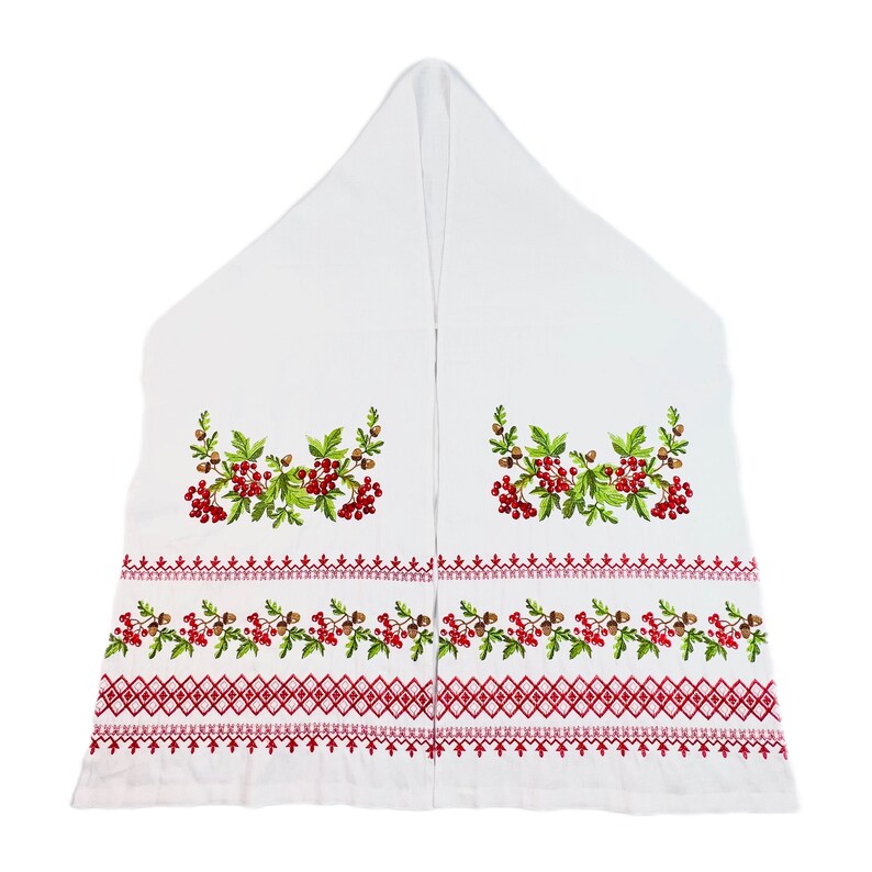 K&ouml;nnte beinhalten: Wei&szlig;es besticktes Textil mit roten Beeren, gr&uuml;nen Bl&auml;ttern und braunen Eicheln. Das Design umfasst einen roten geometrischen Rand. Das Textil ist dreieckig gefaltet, wahrscheinlich ein dekoratives St&uuml;ck.