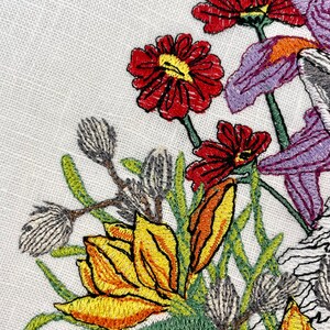 May include: Embroidered floral design featuring yellow, orange, and red flowers with green leaves and stems on a white background.