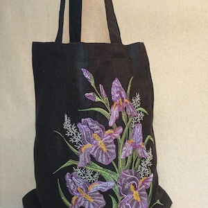 May include: Black tote bag featuring an embroidered design of purple iris flowers with green leaves and stems.