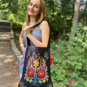 May include: A black tote bag with colorful embroidered flowers. The bag has red tassels on the sides.