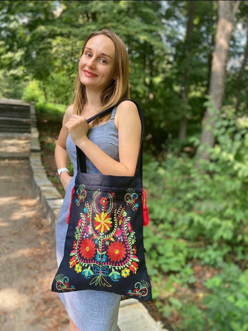 May include: A black tote bag with colorful embroidered flowers. The bag has red tassels on the sides.