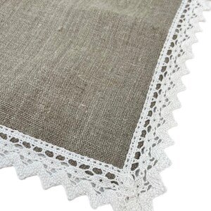 May include: A beige linen tablecloth with a white lace border. The tablecloth has embroidered colorful Easter eggs.
