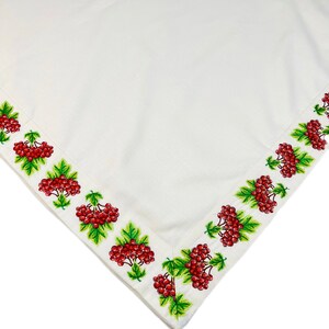 May include: White tablecloth with a detailed embroidered border featuring clusters of red berries and green leaves. The embroidery is on the edge of the cloth, creating a decorative frame.