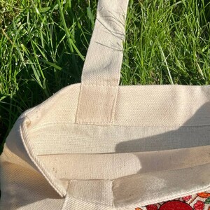 May include: A natural canvas tote bag with a floral embroidery design in shades of red, orange, yellow, and green. The bag has a single strap and is made of a sturdy fabric.