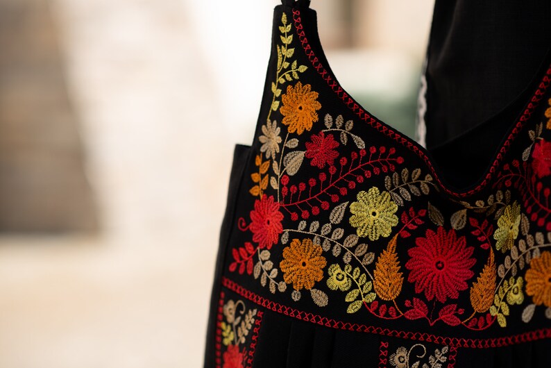 May include: Black shoulder bag with vibrant floral embroidery in red, orange, and yellow. The bag features a detailed design of flowers and leaves, with a contrasting red stitched border. The strap is also black.