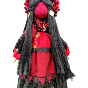 Puede incluir: Una mu&ntilde;eca de tela roja con cabello negro, que lleva un vestido rojo con ribete de encaje negro y una corona de flores rojas en la cabeza.