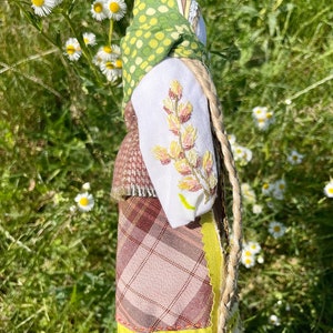 Puede incluir: Una mu&ntilde;eca hecha a mano con un pa&ntilde;uelo de lunares verdes y amarillos, una camisa blanca con flores bordadas, una falda de cuadros marrones y una larga trenza rubia.