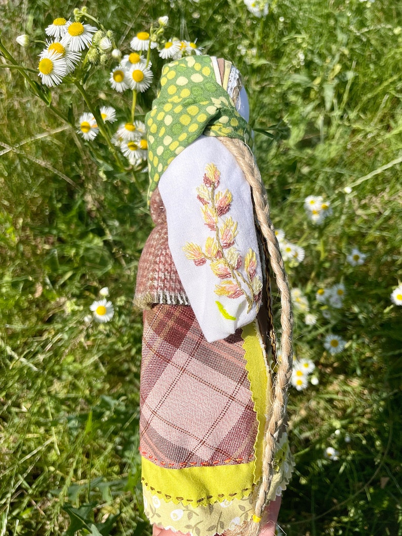 Puede incluir: Una mu&ntilde;eca hecha a mano con un pa&ntilde;uelo de lunares verdes y amarillos, una camisa blanca con flores bordadas, una falda de cuadros marrones y una larga trenza rubia.