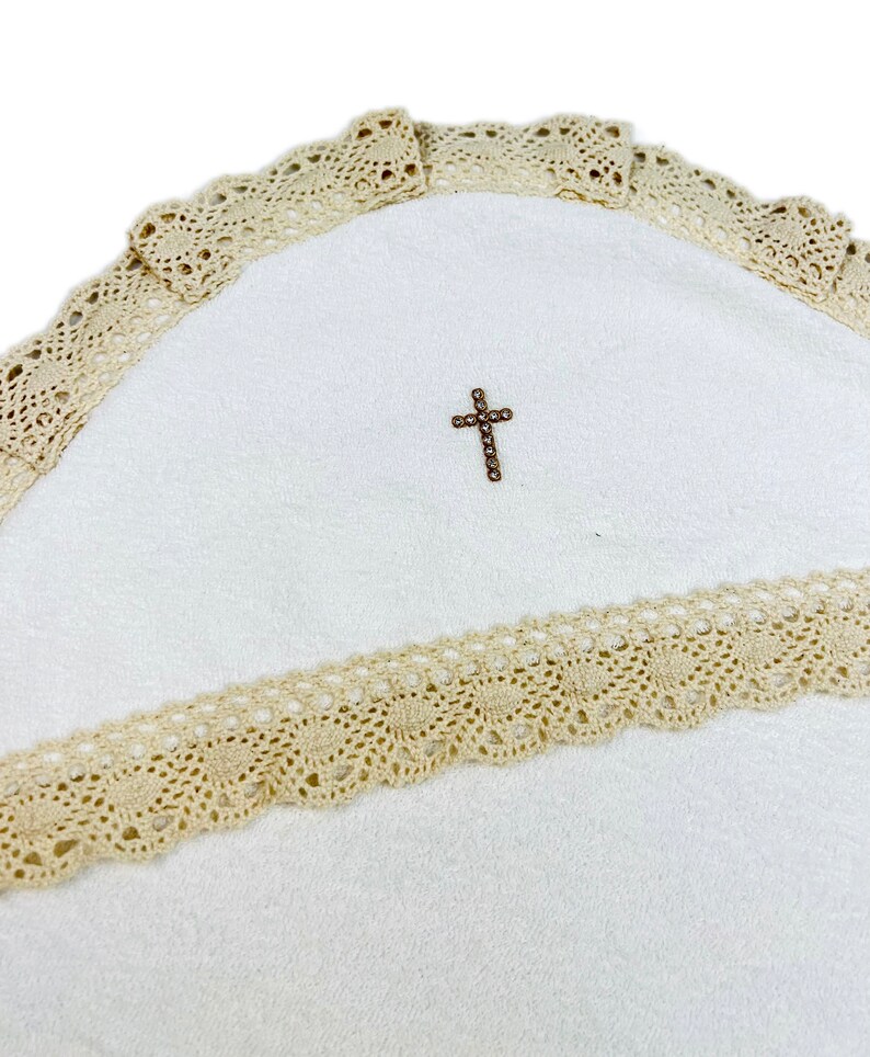 Op de afbeelding: Wit babydekentje met een beige gehaakte rand en een klein gouden kruis in het midden.