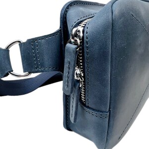 May include: A dark blue leather fanny pack with a silver zipper and a strap with a metal ring.