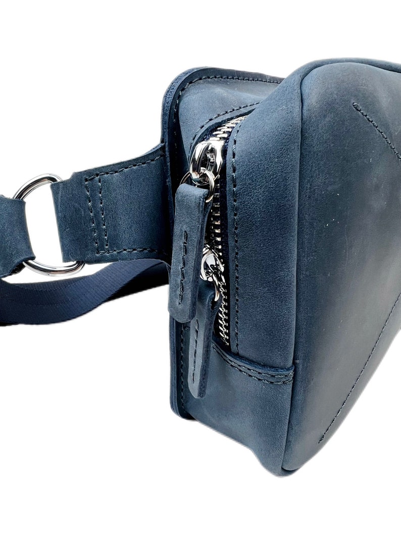 May include: A dark blue leather fanny pack with a silver zipper and a strap with a metal ring.