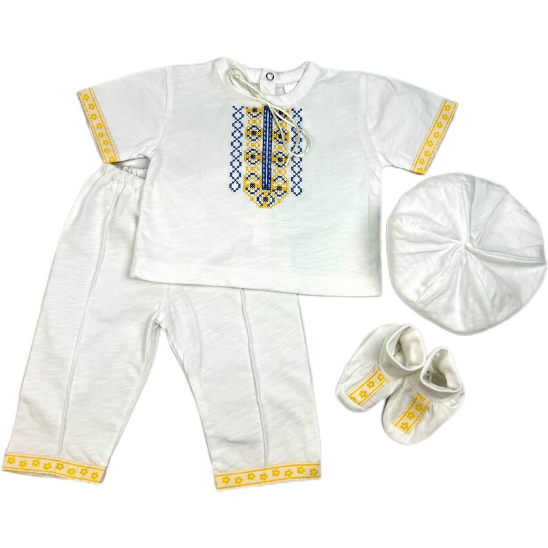 May include: A white baby outfit with yellow and blue embroidery. The outfit includes a shirt, pants, a hat, and booties.