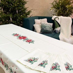 May include: White tablecloth with a red and green holly and poinsettia design. The tablecloth is set with matching napkins and a runner. The text "Walking in a winter wonderland" is on a cushion in the background.
