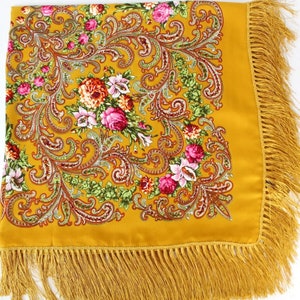 May include: A yellow silk scarf with a floral pattern and gold fringe. The scarf features a paisley design with pink, red, and green flowers.