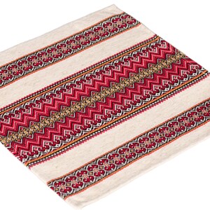 Op de afbeelding: Cr&egrave;mekleurig vierkant textiel met een gestreept ontwerp. De strepen hebben ingewikkelde rode en gouden geometrische patronen, waardoor een levendig contrast ontstaat met de neutrale achtergrond. Het textiel lijkt van geweven stof te zijn.