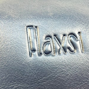 May include: Close-up of a black leather surface with the word "Playsi" embossed in silver lettering.
