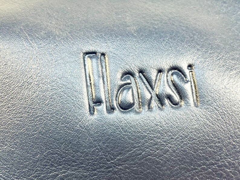 May include: Close-up of a black leather surface with the word "Playsi" embossed in silver lettering.