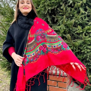 May include: A woman wearing a black coat with a fur collar and a red shawl with floral embroidery and fringe. The shawl is draped over her shoulders and has a traditional design.
