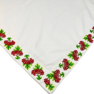 May include: White tablecloth with a detailed border featuring clusters of red berries and green leaves. The embroidered design frames the edge of the cloth, creating a decorative accent. The fabric has a subtle texture.
