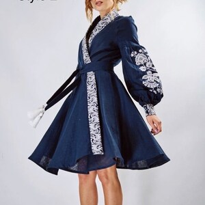 May include: A navy blue linen dress with white embroidery. The dress has a wrap style and a belt with white embroidery. The dress has long sleeves with white embroidery on the cuffs. The dress has a flared skirt. The dress is labelled "Style 2".