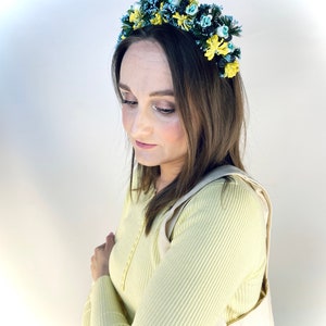 Pode incluir: Uma mulher vestindo um su&eacute;ter amarelo e uma faixa de cabe&ccedil;a floral com flores azuis e amarelas. A faixa de cabe&ccedil;a &eacute; feita de tecido e tem uma arma&ccedil;&atilde;o de arame.