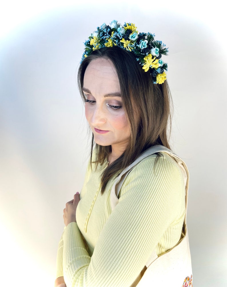 Pode incluir: Uma mulher vestindo um su&eacute;ter amarelo e uma faixa de cabe&ccedil;a floral com flores azuis e amarelas. A faixa de cabe&ccedil;a &eacute; feita de tecido e tem uma arma&ccedil;&atilde;o de arame.