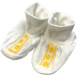 May include: A pair of white baby booties with yellow flower trim.