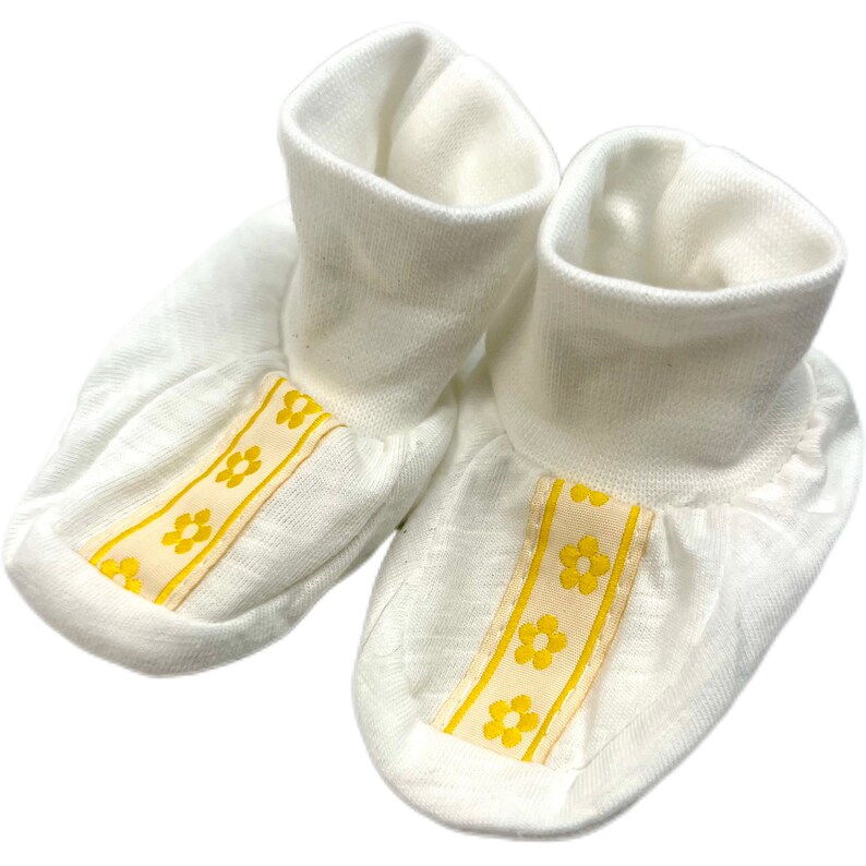 May include: A pair of white baby booties with yellow flower trim.