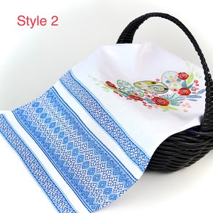 May include: White linen towel with blue geometric border and embroidered Easter egg design. The towel is draped over a black wicker basket. The text "Style 2" is in the upper left corner.