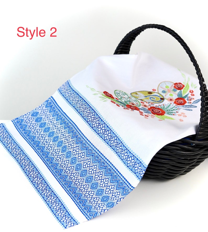 May include: White linen towel with blue geometric border and embroidered Easter egg design. The towel is draped over a black wicker basket. The text "Style 2" is in the upper left corner.