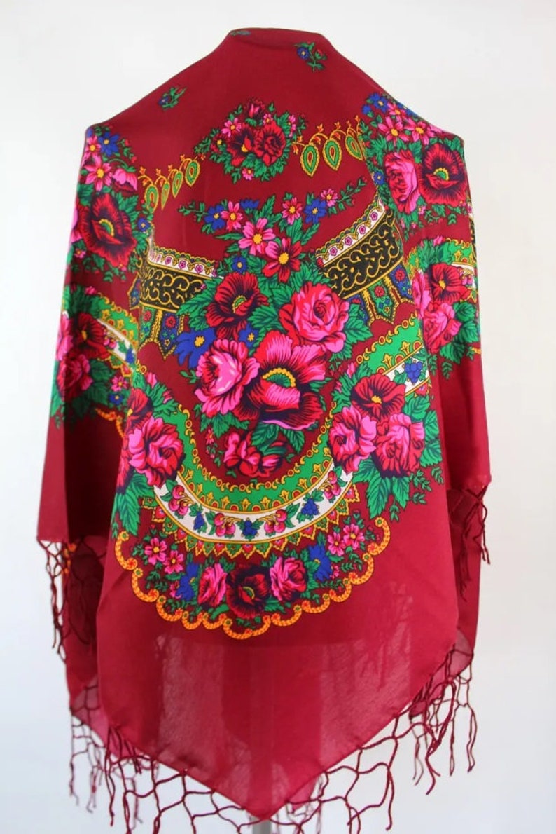 Puede incluir: Una bufanda roja con estampado floral y borde de flecos. La bufanda presenta un dise&ntilde;o circular con flores rosas, rojas, verdes, azules y amarillas.