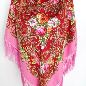 Pu&ograve; includere: Un foulard di seta rosso e rosa con motivi floreali e accenti dorati. Il foulard ha frange rosa sui bordi.