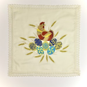 Pu&ograve; includere: Un asciugamano da cucina bianco ricamato con un bordo all'uncinetto presenta un gallo e uova colorati. Il gallo &egrave; marrone, giallo e rosso, e le uova sono blu, gialle e bianche.
