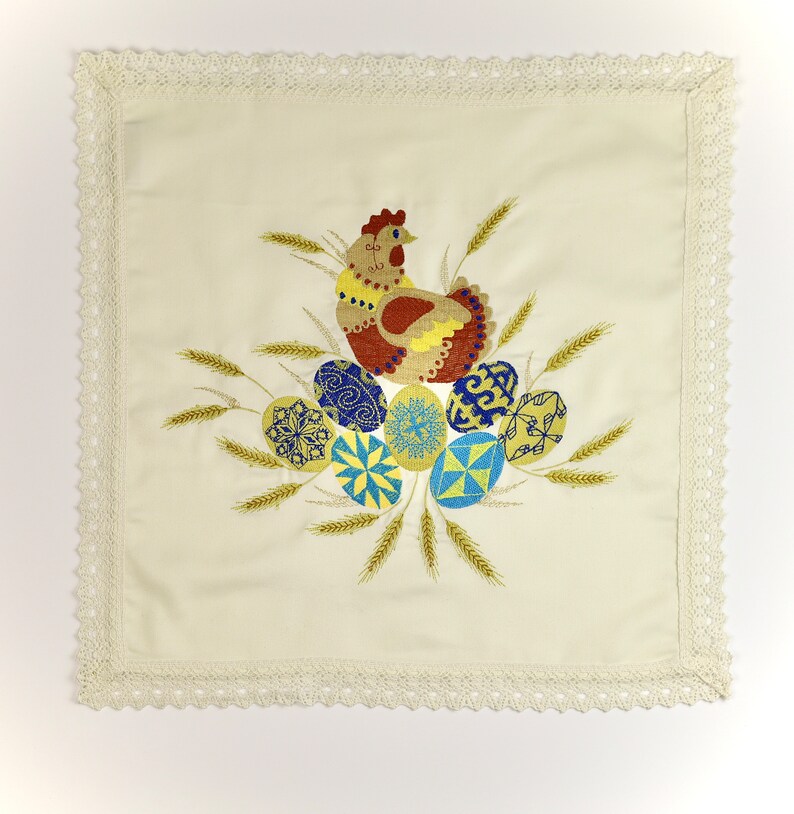 Pu&ograve; includere: Un asciugamano da cucina bianco ricamato con un bordo all'uncinetto presenta un gallo e uova colorati. Il gallo &egrave; marrone, giallo e rosso, e le uova sono blu, gialle e bianche.