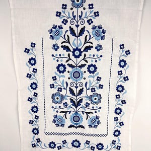 May include: A white rectangular textile featuring intricate embroidery in shades of dark blue, medium blue, and light blue. The design consists of a central vertical floral arrangement flanked by two side borders of small flowers and vines.