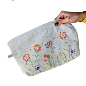 May include: A beige canvas pouch with a zipper closure and a floral embroidery design. The embroidery features colorful flowers in shades of orange, red, blue, and green.