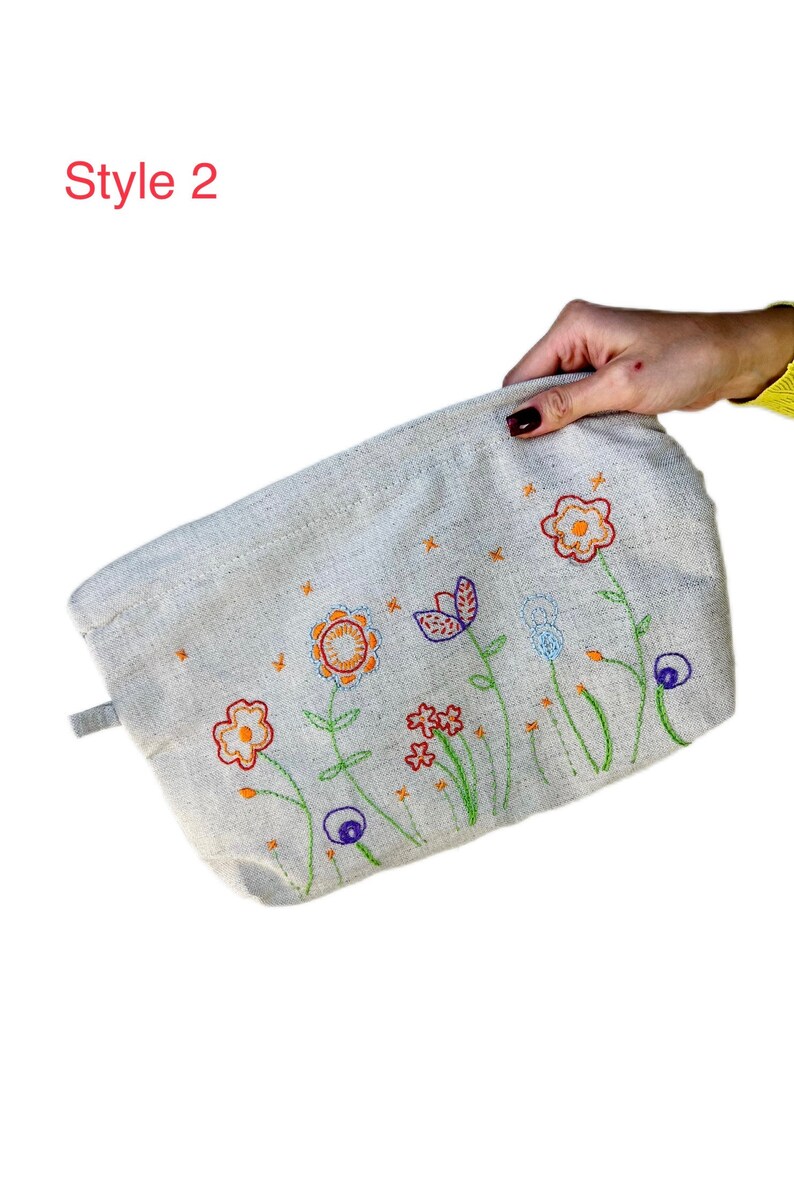 May include: A beige canvas pouch with a zipper closure and a floral embroidery design. The embroidery features colorful flowers in shades of orange, red, blue, and green.